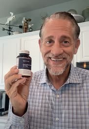Man holding a bottle of supplements in a kitchen.
