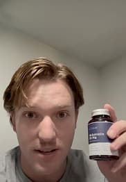Person holding a bottle labeled 'Melatonin 10 mg' in a room.
