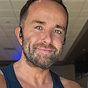 A man with short brown hair, a beard, and blue eyes is smiling at the camera.