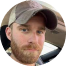 A person with a beard wearing a cap inside a car.
