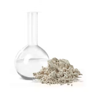 Glass flask with clear liquid beside a pile of gray powder.