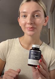 Person holding a bottle of supplements, smiling at the camera.