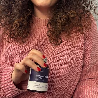 Person holding a bottle of melatonin, wearing a pink sweater.