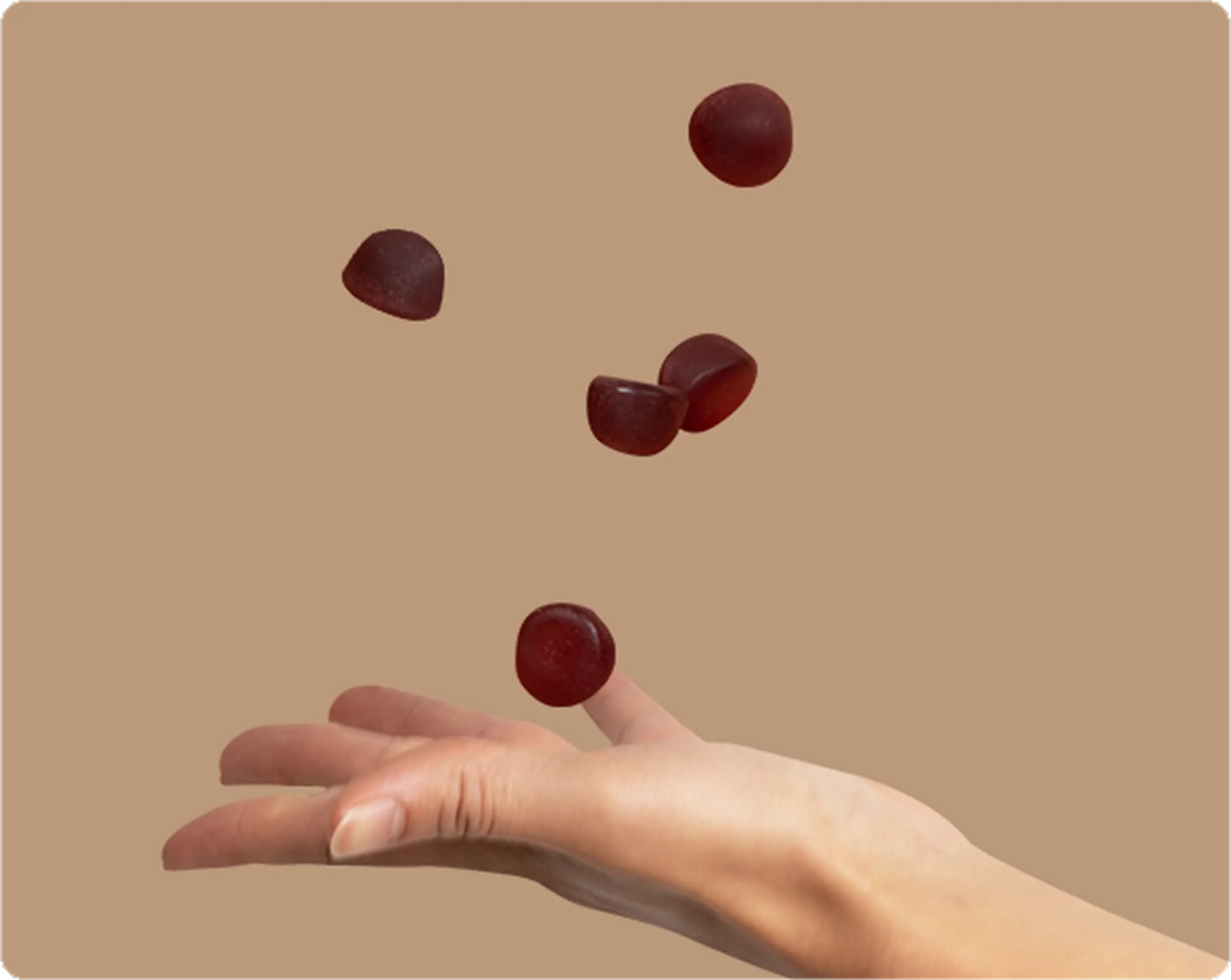 A hand catching falling red gummy candies on a beige background.