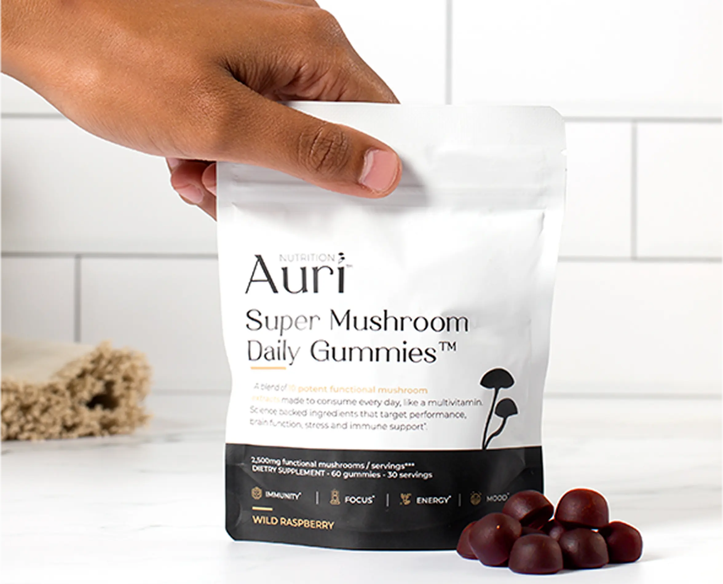 Hand holding a bag of Auri Super Mushroom Daily Gummies with gummies on a table.