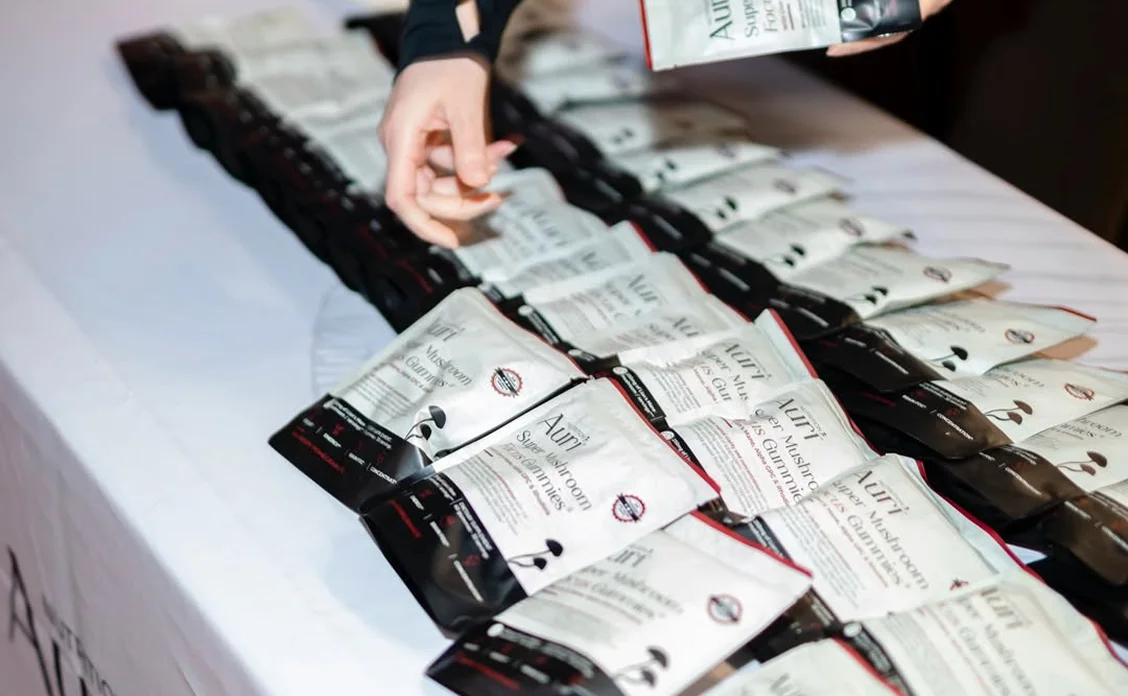 A person's hand reaches for a packet of Auri mushroom gummies from a large display on a table.