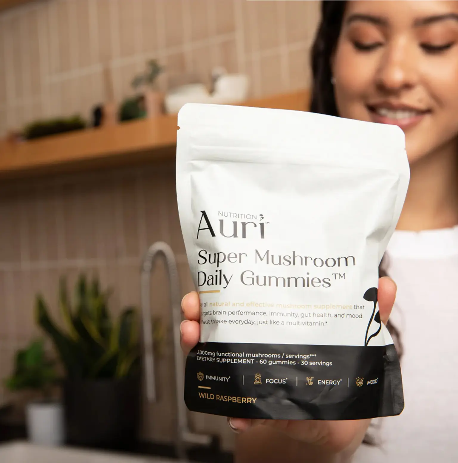 Person holding a bag of Auri Super Mushroom Daily Gummies in a kitchen.