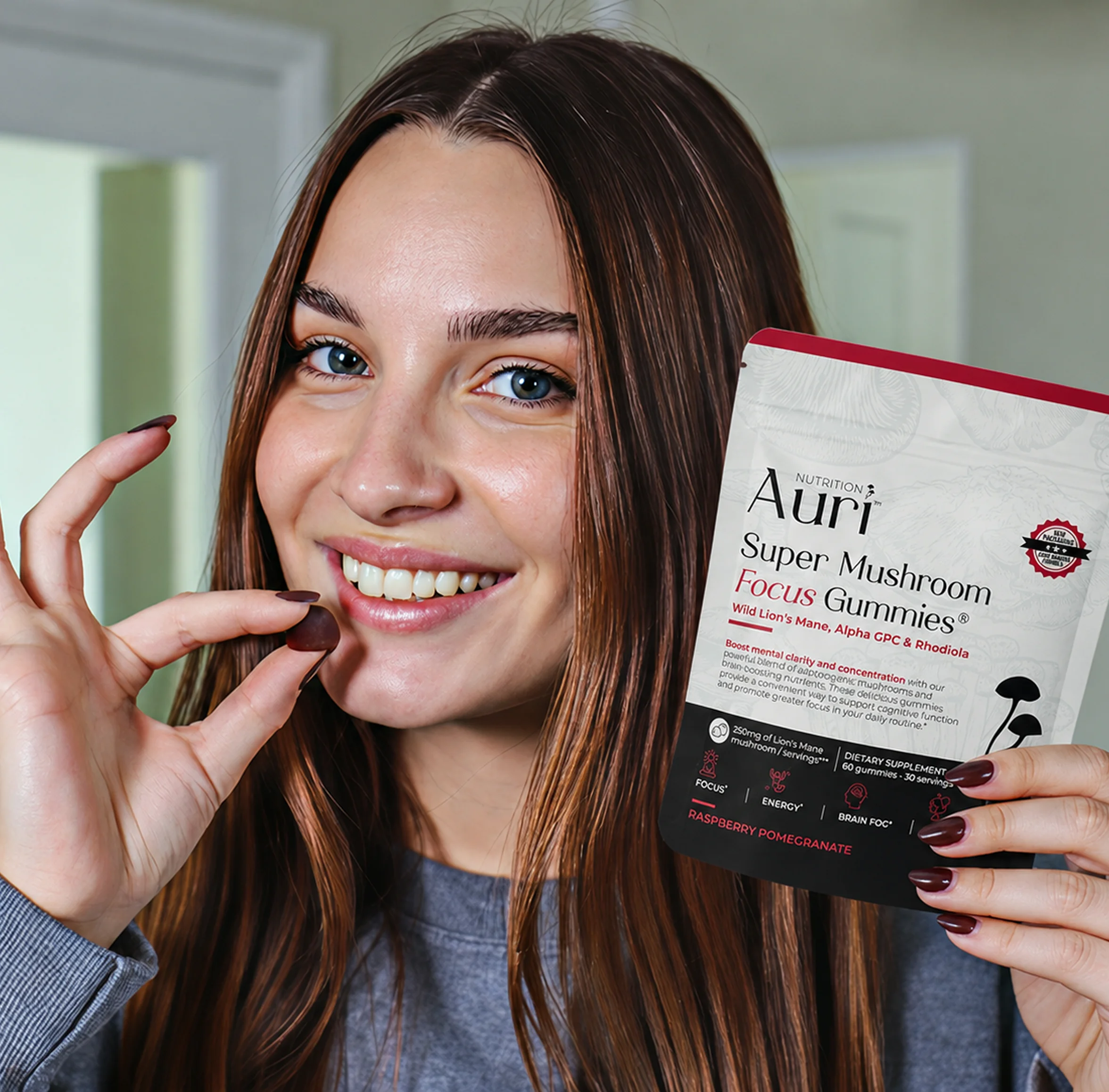 A smiling woman holds a pouch of Auri Super Mushroom Focus Gummies while bringing a gummy to her mouth.