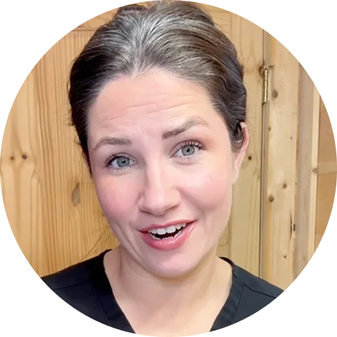 A circular headshot of a smiling woman with graying hair pulled back, standing before a wood-paneled wall.