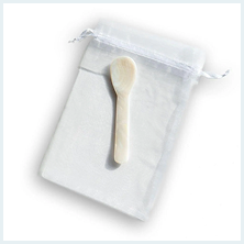 A small, off-white spoon made of shell or bone resting on a white mesh drawstring pouch.