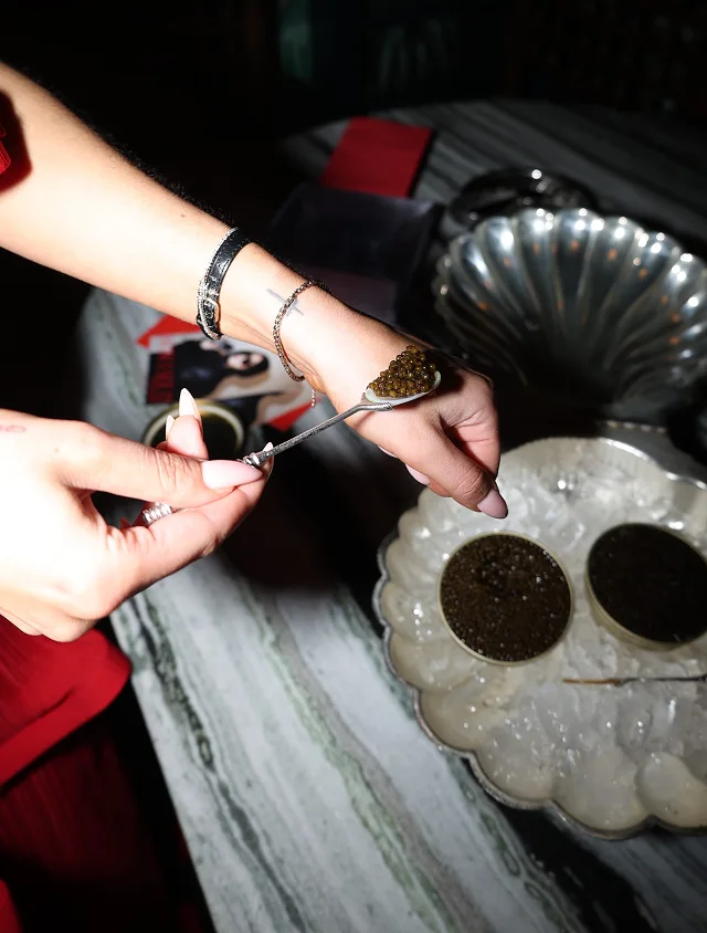 A person eats caviar from a spoon resting on the back of their hand.