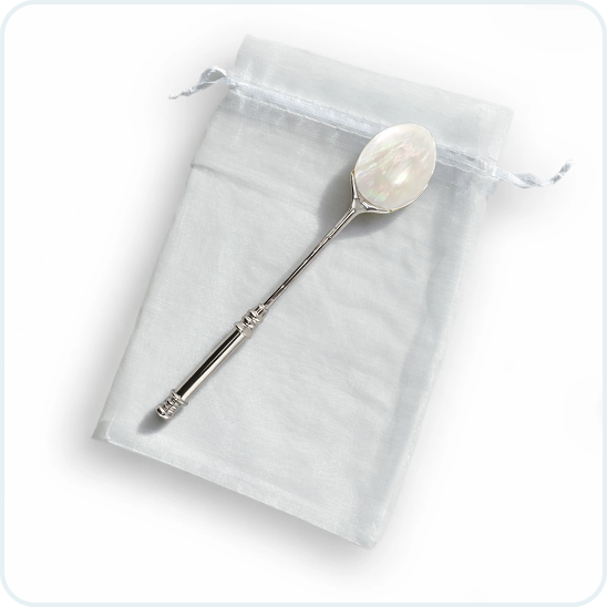 A silver spoon with a mother-of-pearl bowl resting on a small, sheer white drawstring pouch.