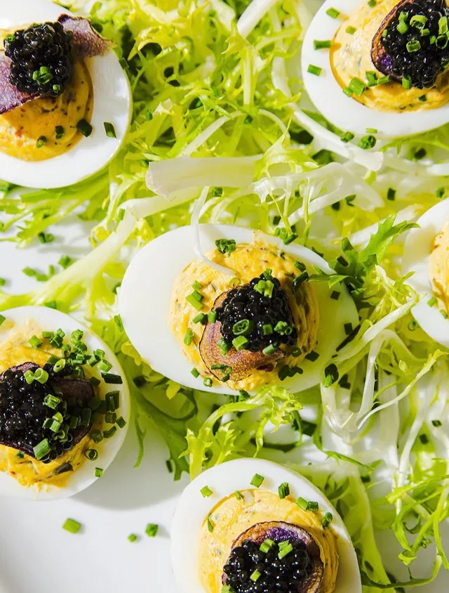 A close-up of deviled eggs topped with black caviar and chives, arranged on a bed of frisée lettuce.