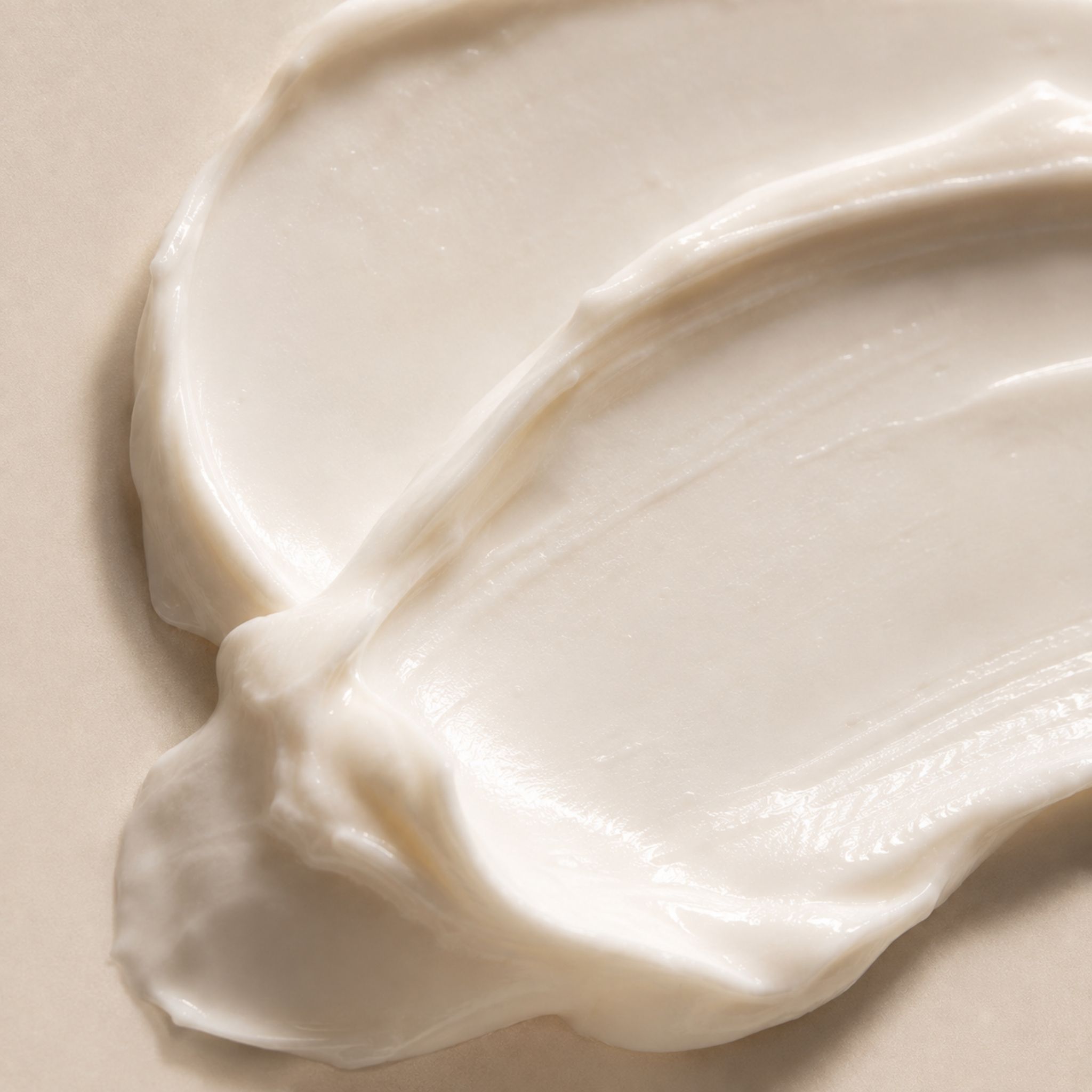 A close-up, textural shot of thick, white cream swirled across a light beige surface.