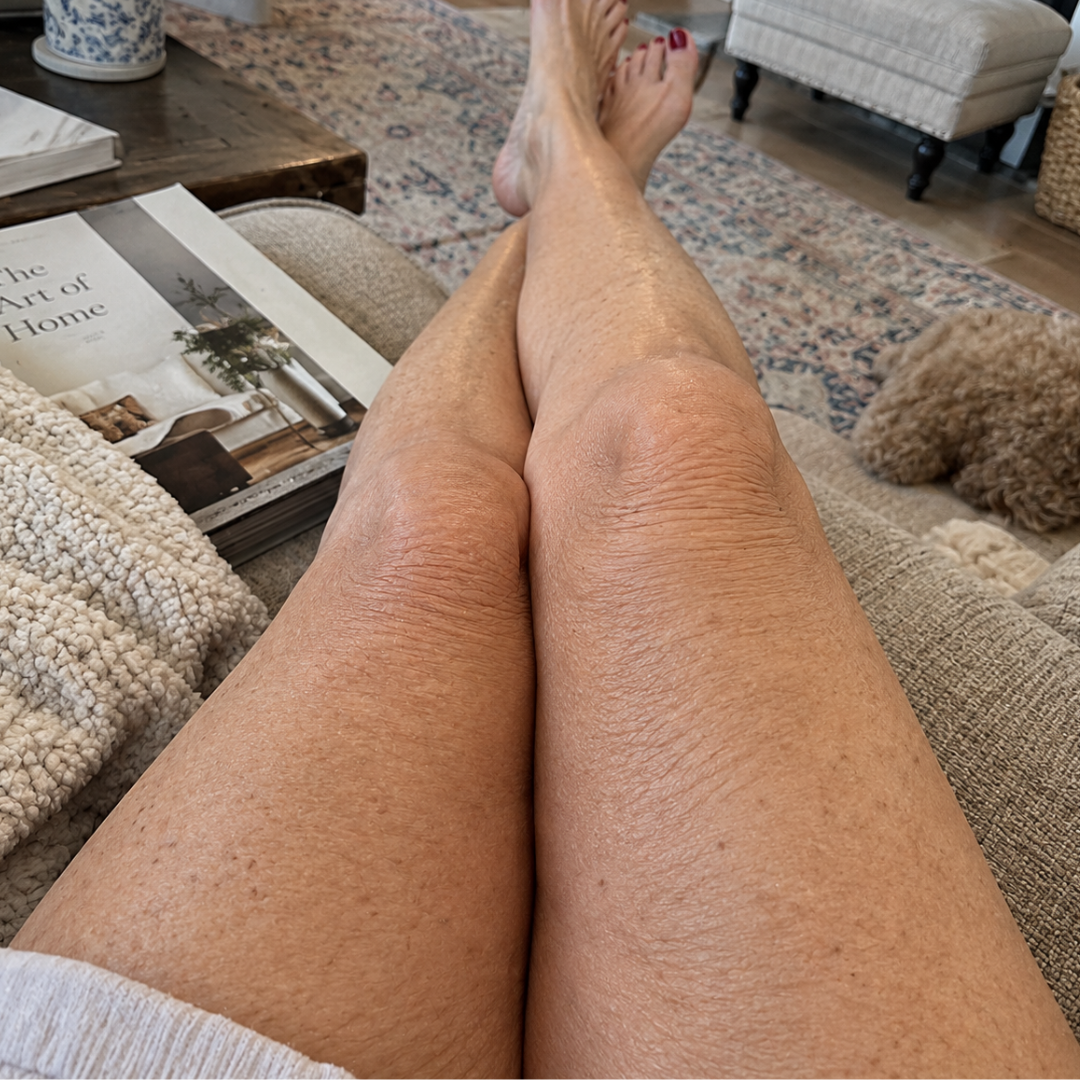 A first-person view of a person's legs crossed while relaxing on a couch with a book nearby.