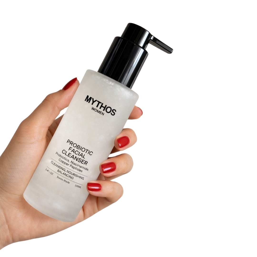 A hand with red nail polish holds a bottle of Mythos Women Probiotic Facial Cleanser against a white background.
