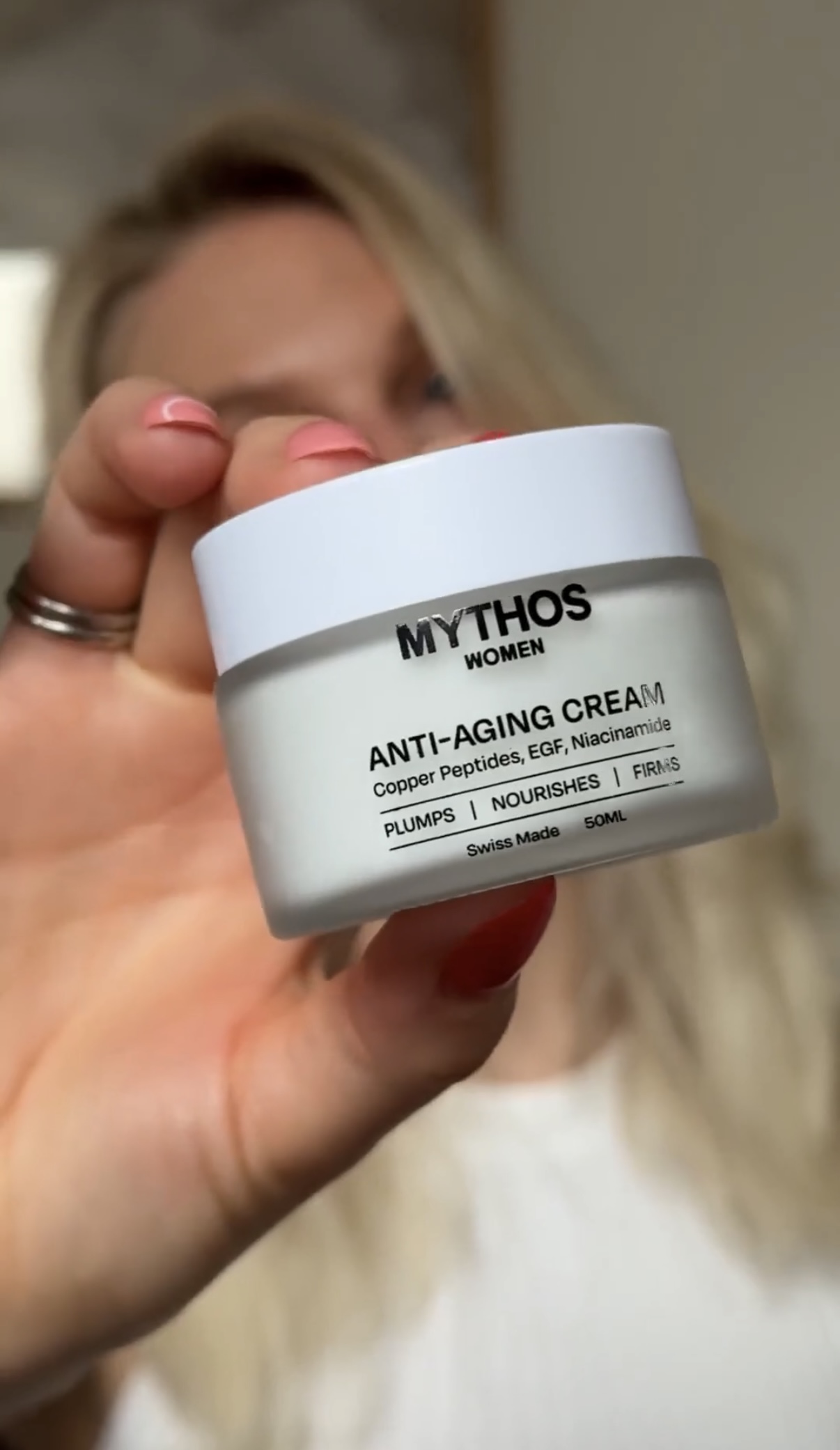 A woman holds a jar of Mythos Women Anti-Aging Cream, with the label facing the camera.