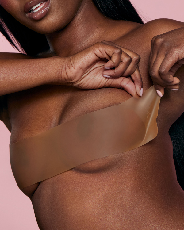 A close-up of a woman applying a wide strip of brown adhesive tape to her chest.