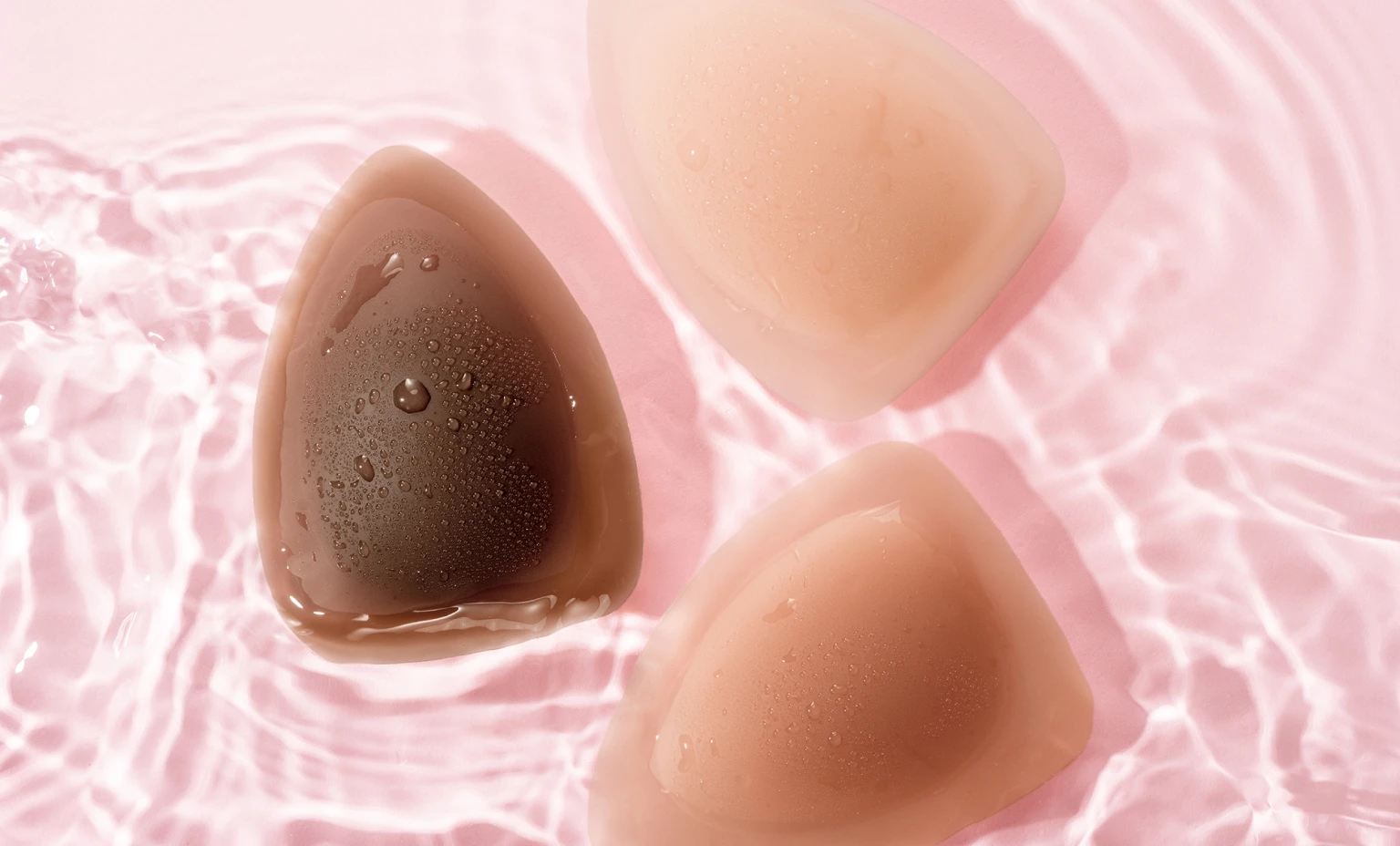 Three silicone bra inserts on a pink, watery surface.
