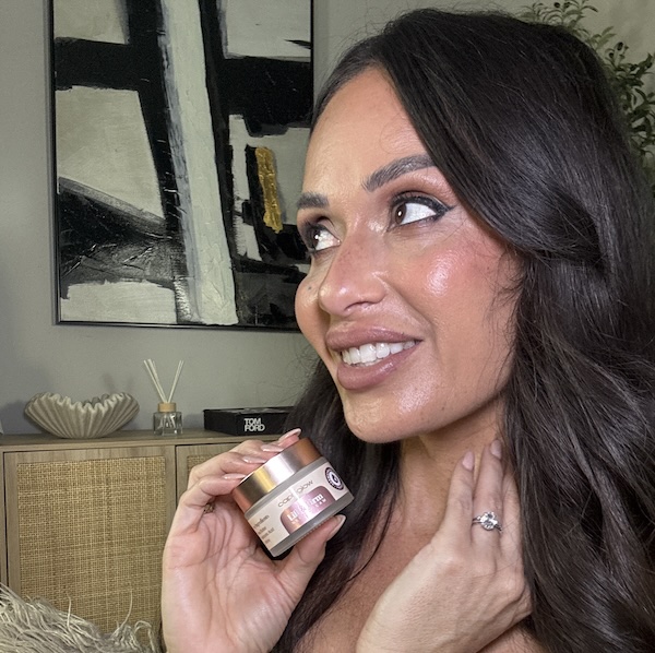 Person holding a jar of skincare cream indoors, with abstract painting in background.