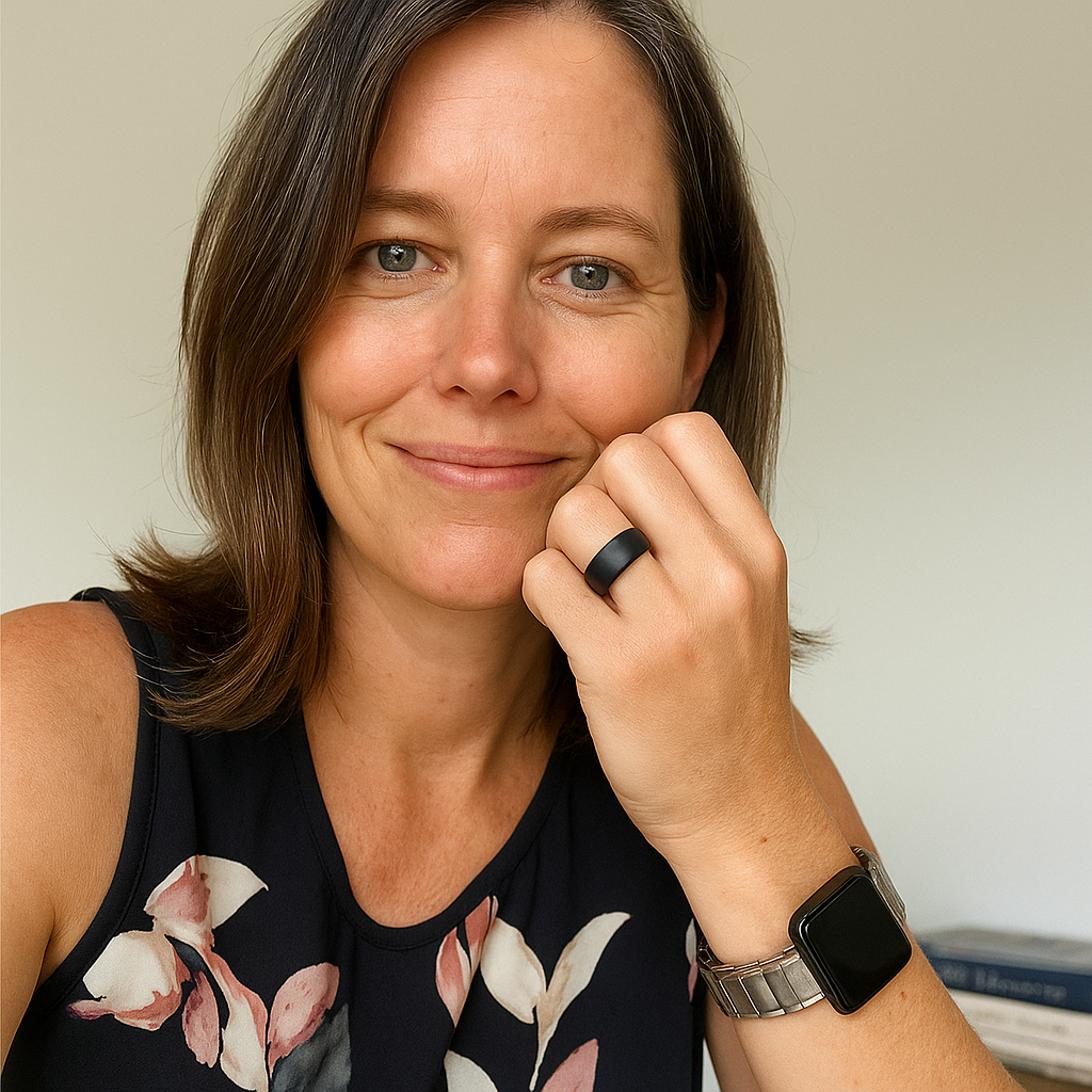 Person smiling, wearing a black ring and smartwatch, in a floral top.
