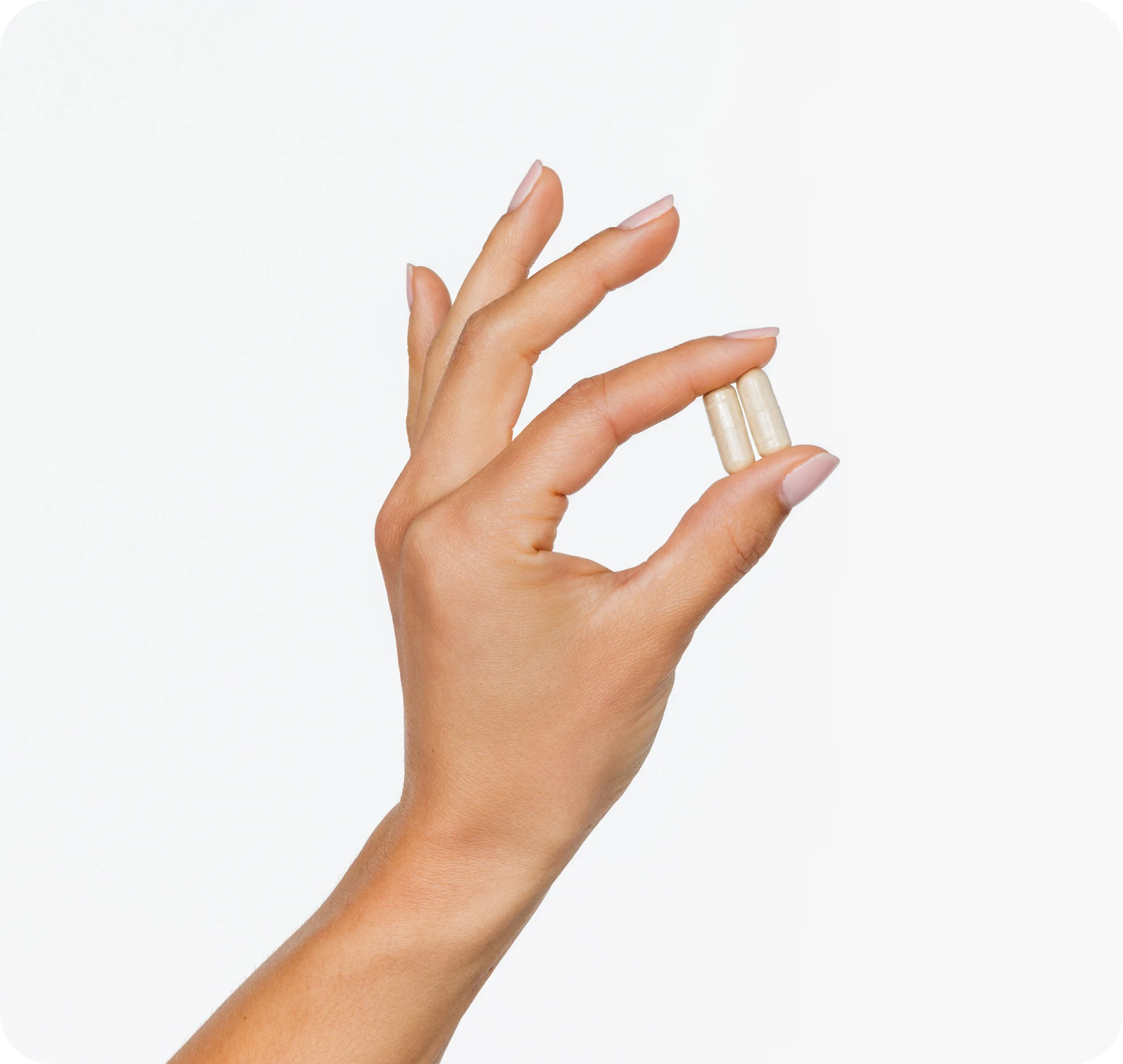 A manicured hand holding two off-white capsules between the thumb and forefinger against a white background.