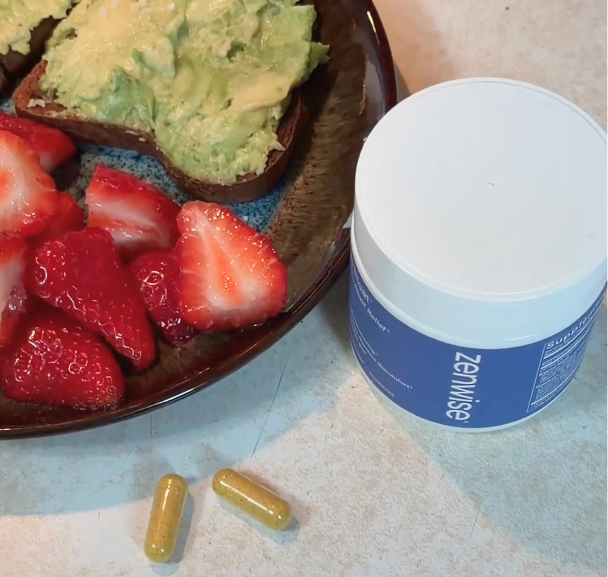 Avocado toast, strawberries, Zenwise jar, and two yellow capsules on a counter.