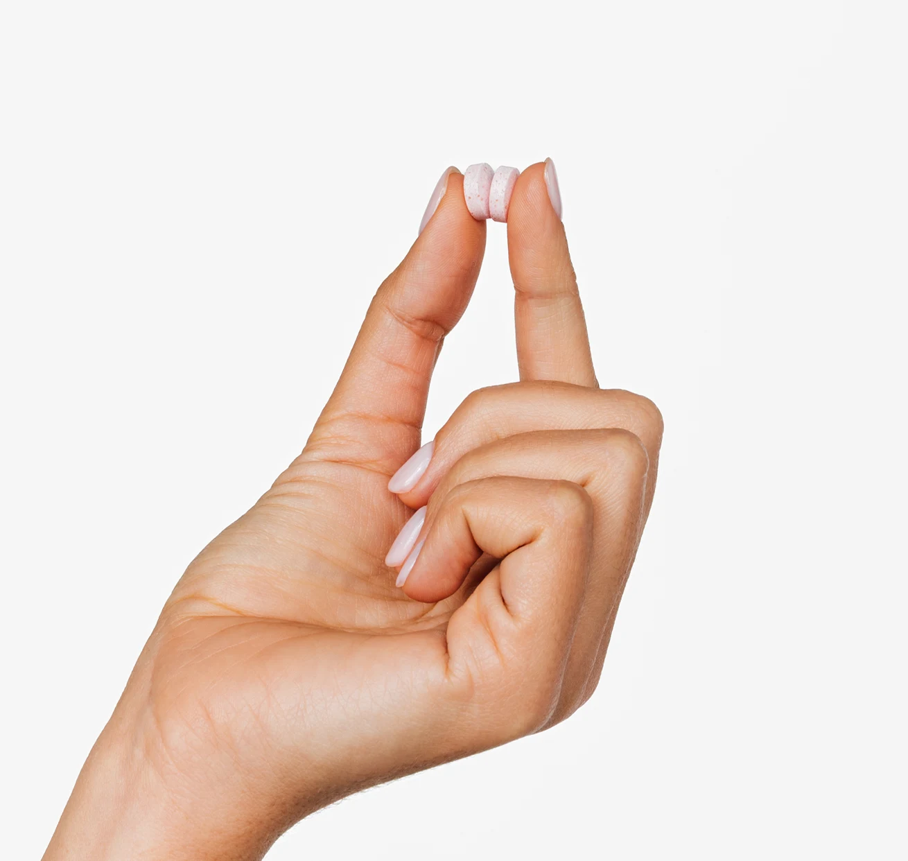 A hand holding three small, pink, circular tablets between the thumb and forefinger against a white background.