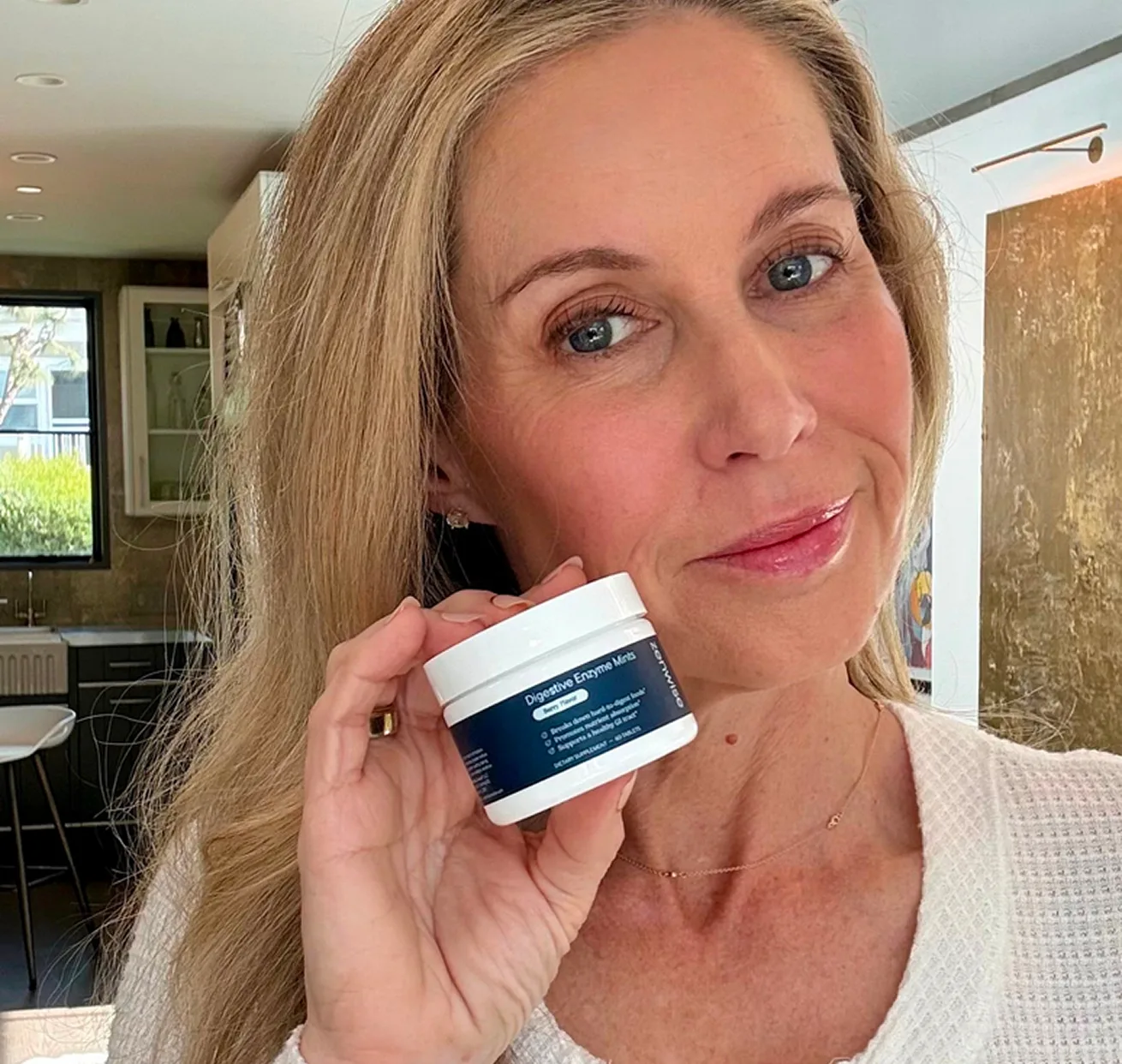 A woman with blonde hair holds up a small white jar labeled 'Digestive Enzyme Mints'.