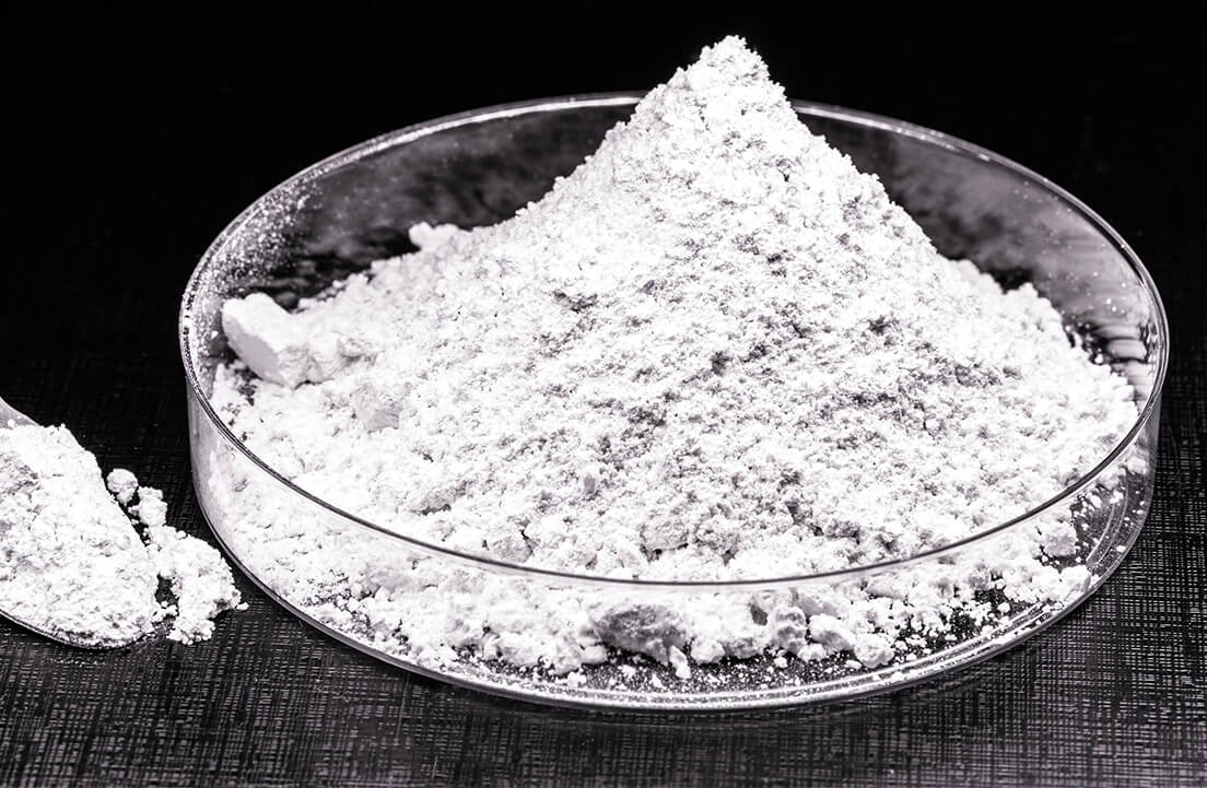 A pile of white powder in a glass dish on a dark surface.