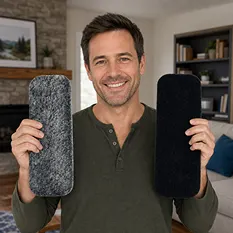 A smiling man holds a gray, fuzzy rectangular pad in one hand and a black one in the other.