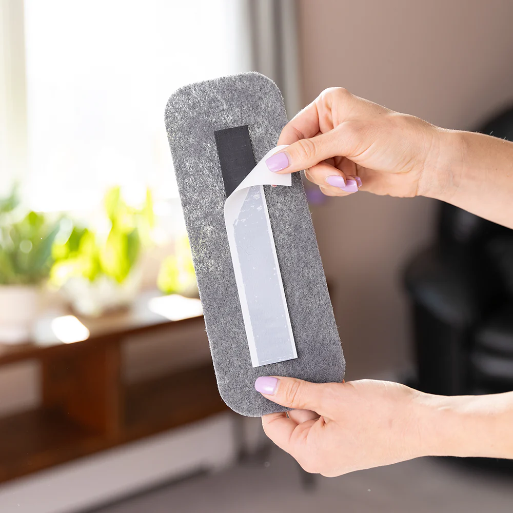 Hands peeling adhesive backing from a gray felt pad.