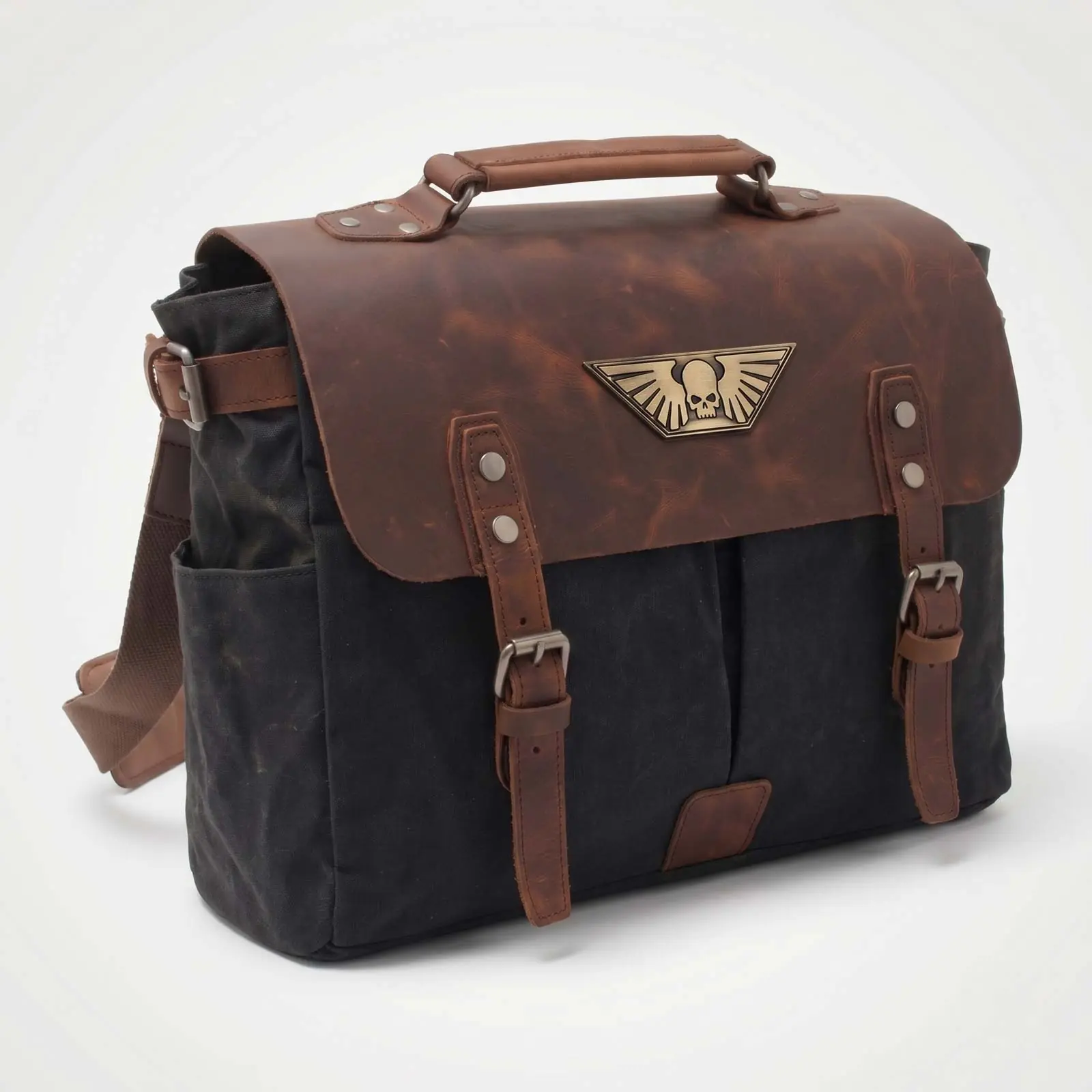 A black canvas messenger bag with a brown leather flap, straps, and a winged skull emblem.