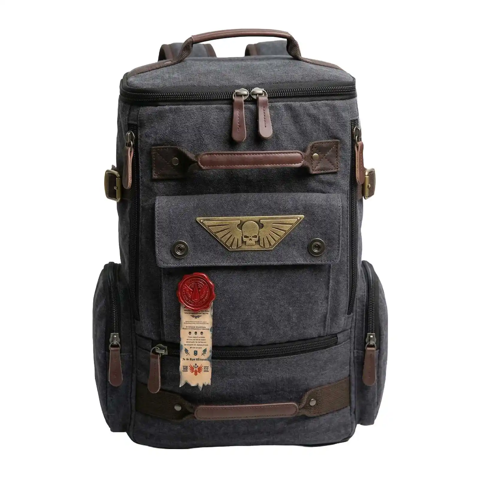 A gray canvas backpack with brown leather trim and a brass winged skull emblem on the front pocket.