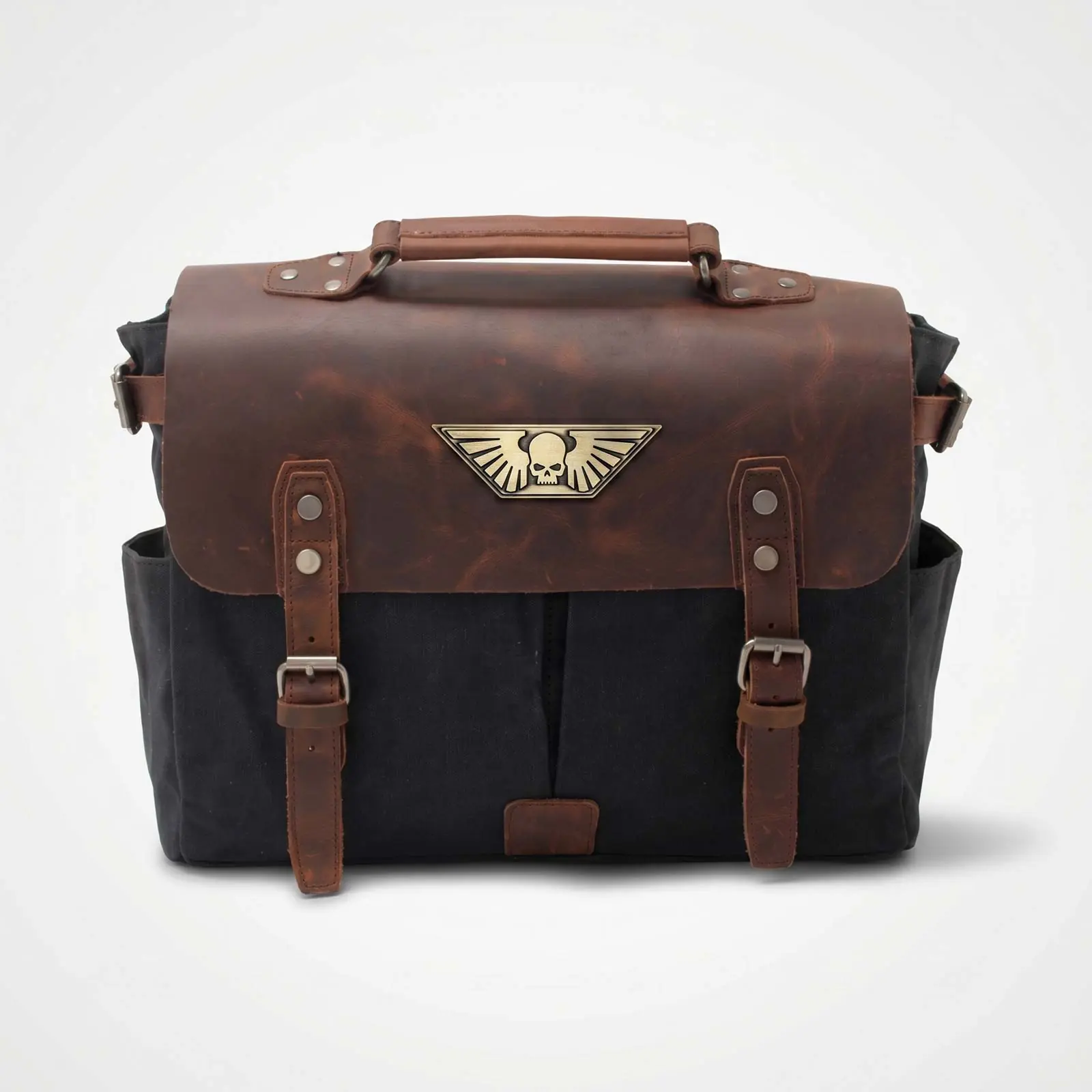 A black canvas and brown leather messenger bag with a metal winged skull emblem on the front.