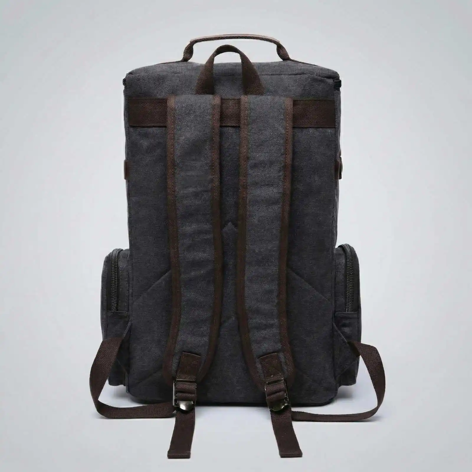The back of a dark grey canvas backpack with brown straps against a plain light grey background.