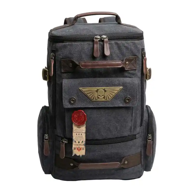 A dark gray canvas backpack with brown leather accents and a bronze winged skull emblem on the front.