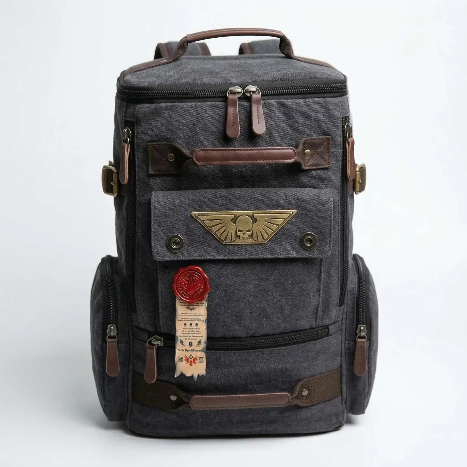 A dark grey canvas backpack with brown leather accents and a brass winged skull emblem on the front.