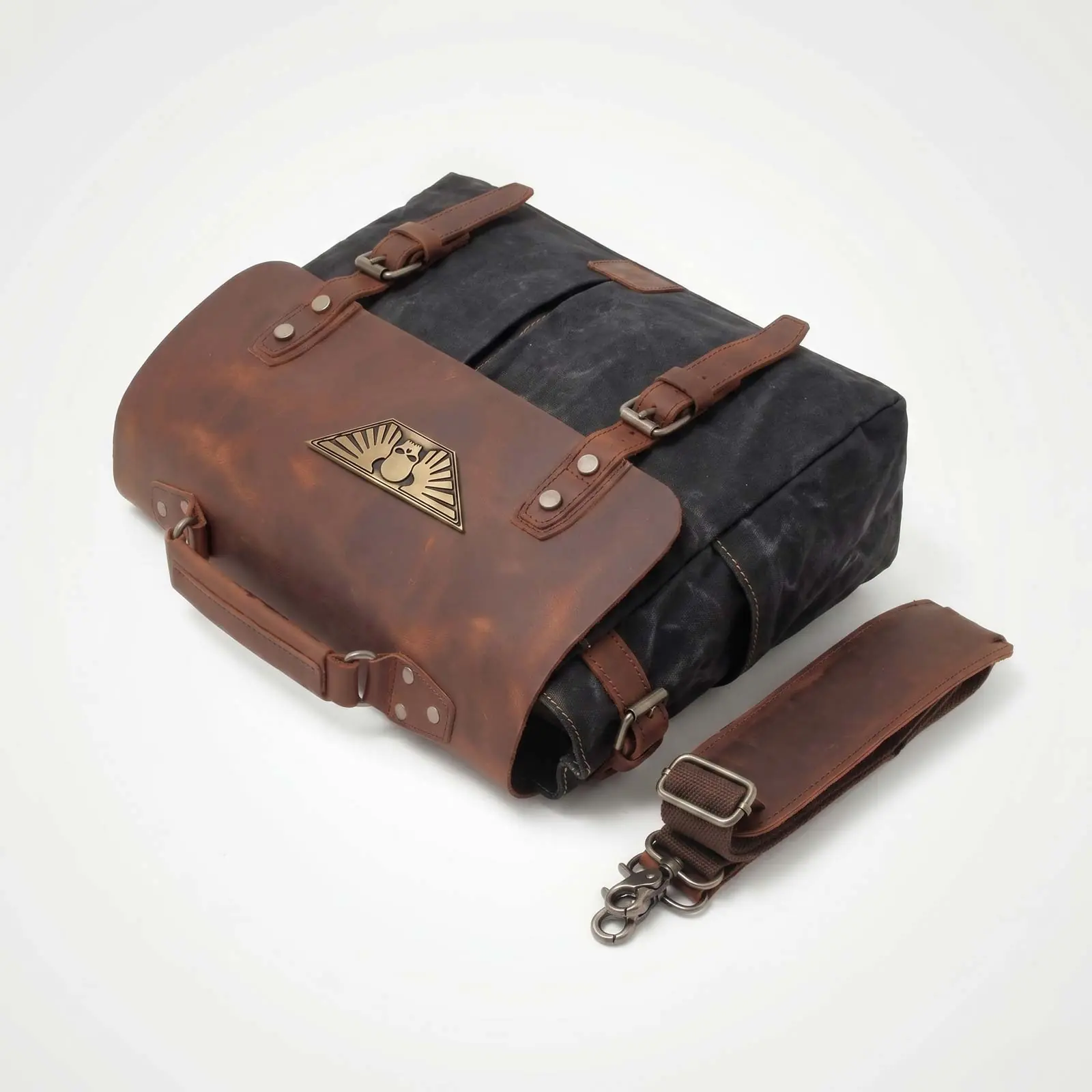 A black canvas messenger bag with a brown leather flap and straps, next to a detached shoulder strap.