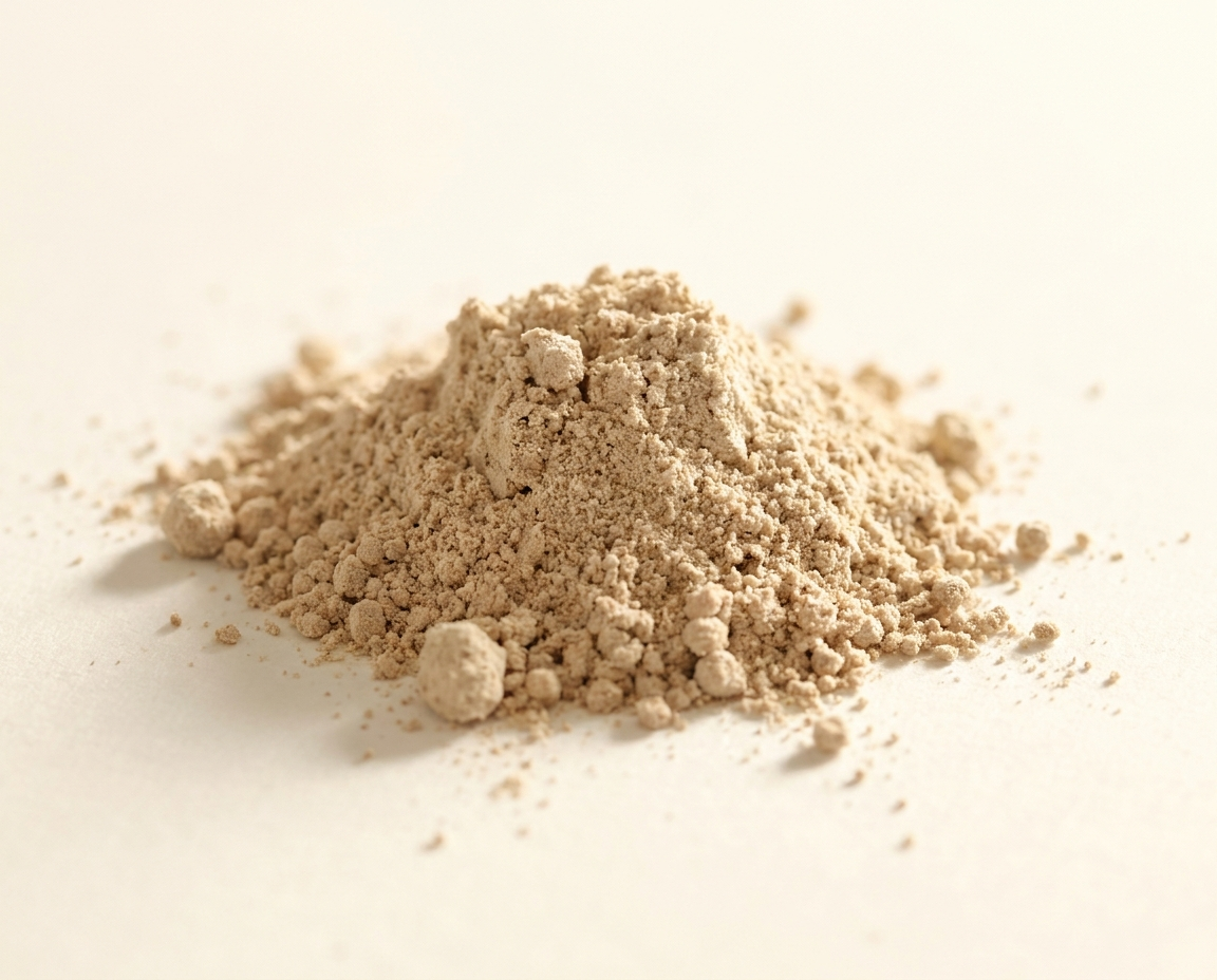 A close-up shot of a small pile of light brown powder on a plain, off-white surface.
