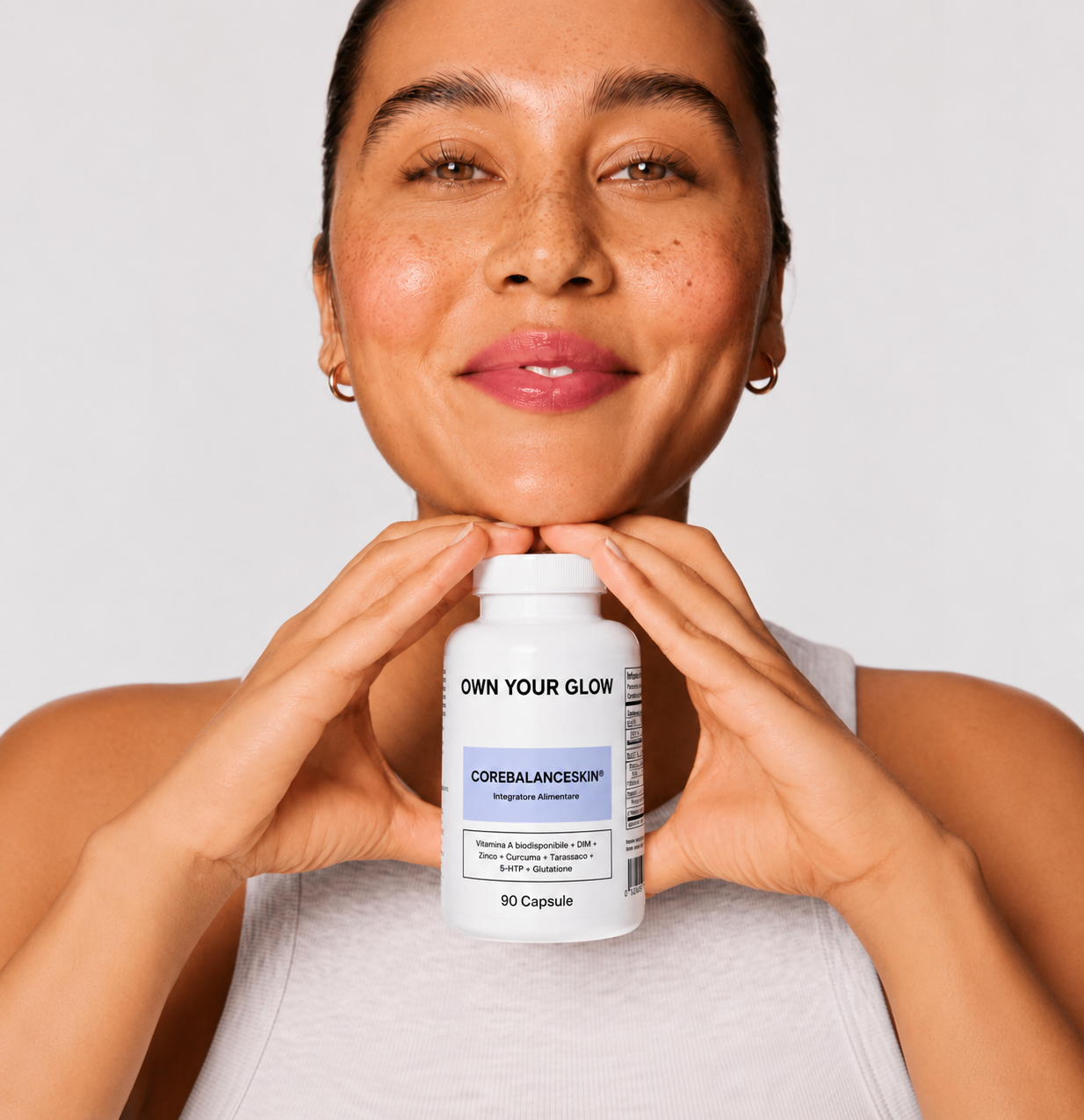 A smiling woman with freckles holds a white bottle of Corebalanceskin supplements under her chin.