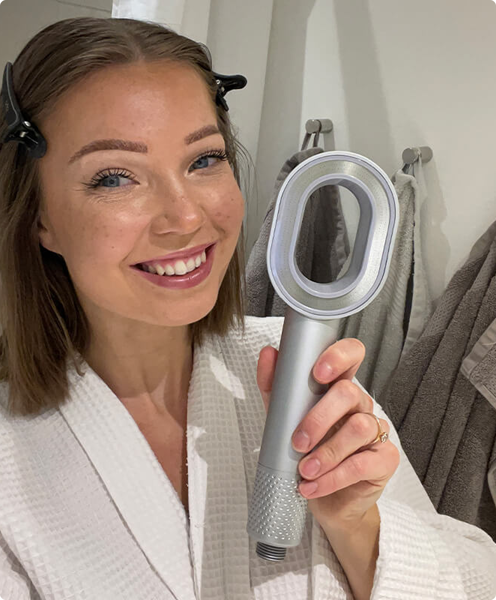 Person in a robe holding a silver hairdryer in a bathroom.