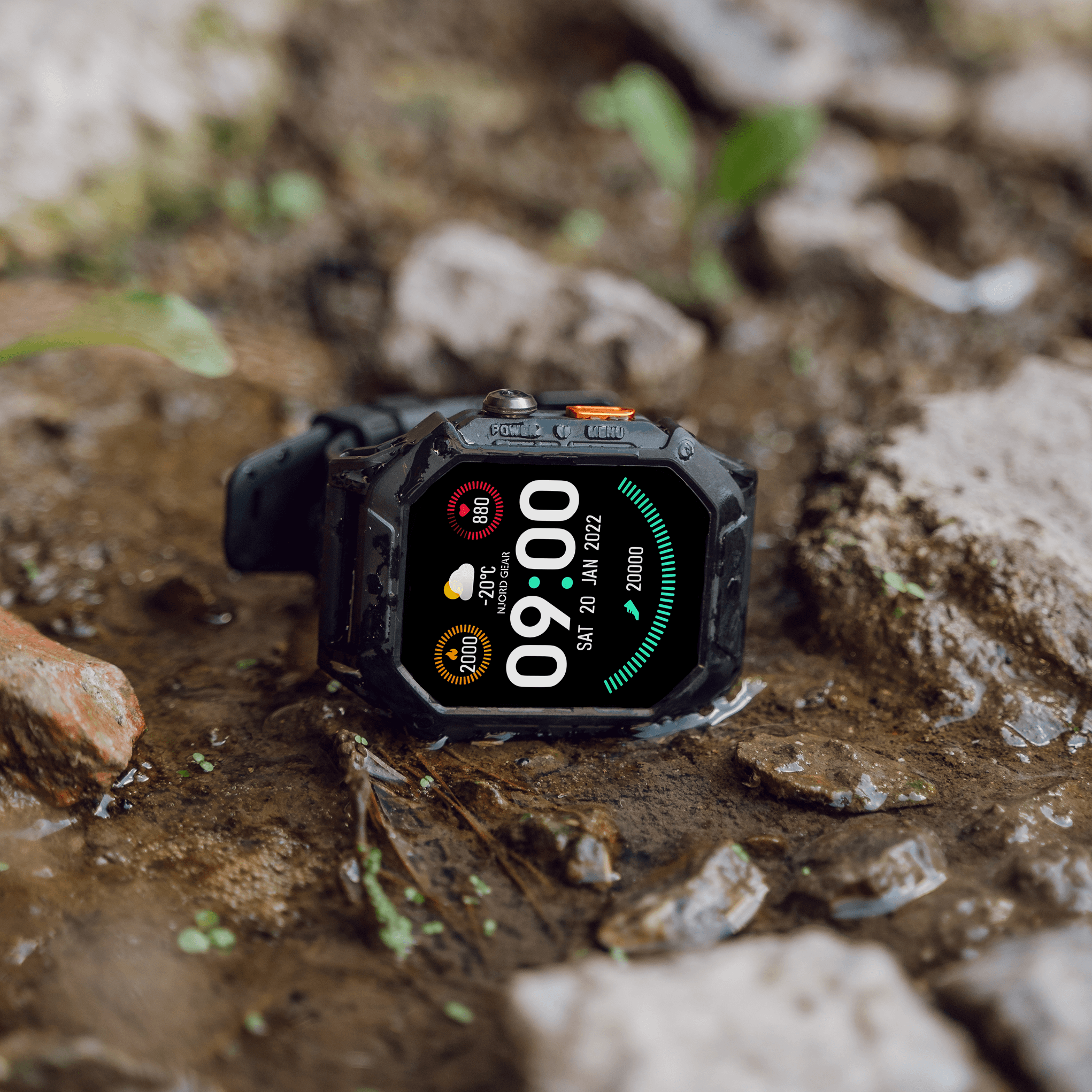 A rugged smartwatch displaying time and weather, lying on wet ground.