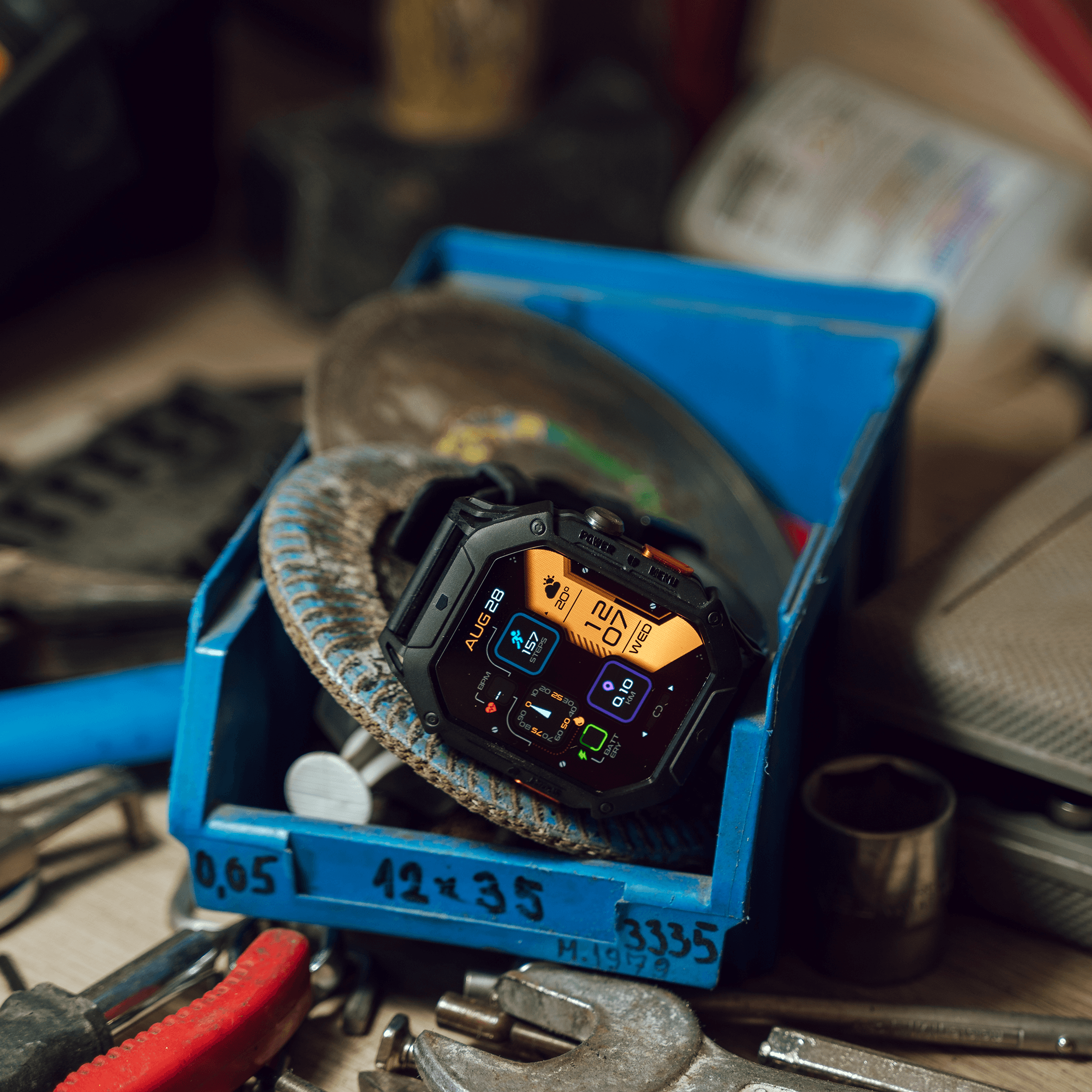 Smartwatch with orange display in a blue box surrounded by tools.