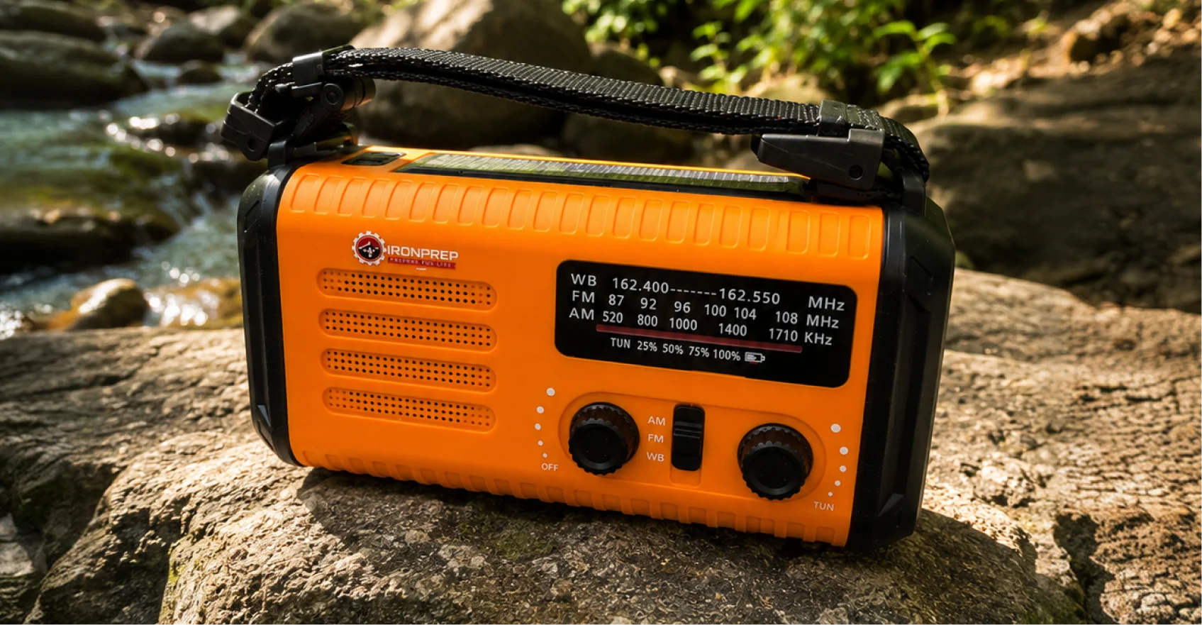 An orange and black emergency radio sits on a rock next to a stream in the woods.