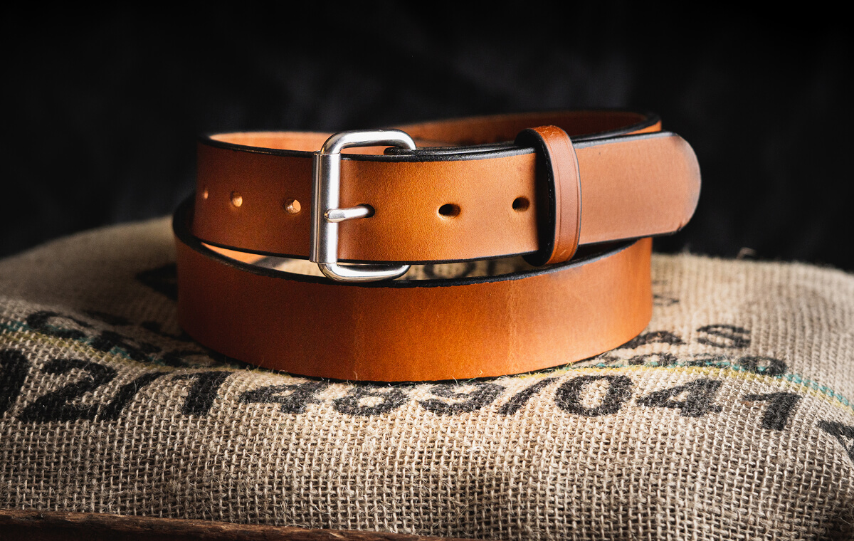 A brown leather belt with a silver buckle on burlap fabric.