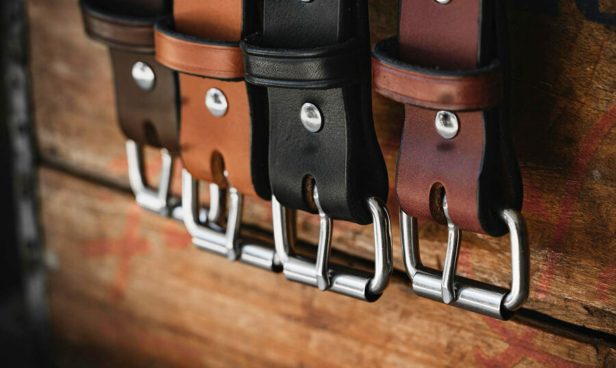 Several leather belts with shiny metal buckles hanging on a wooden surface.