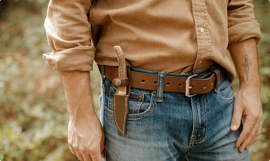 Man wearing a brown shirt and jeans with a knife in belt sheath.