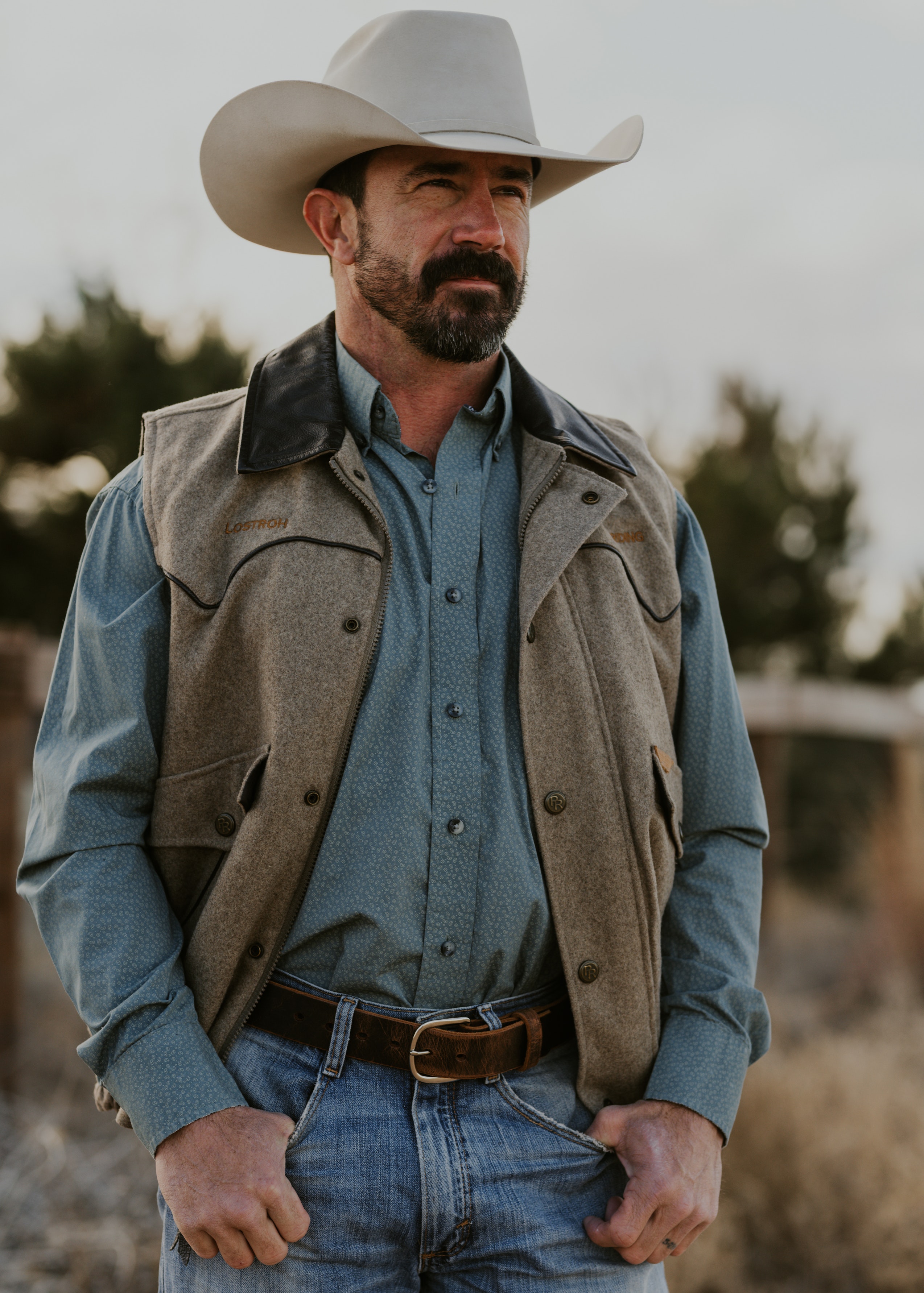 Man in cowboy hat and vest standing outdoors.
