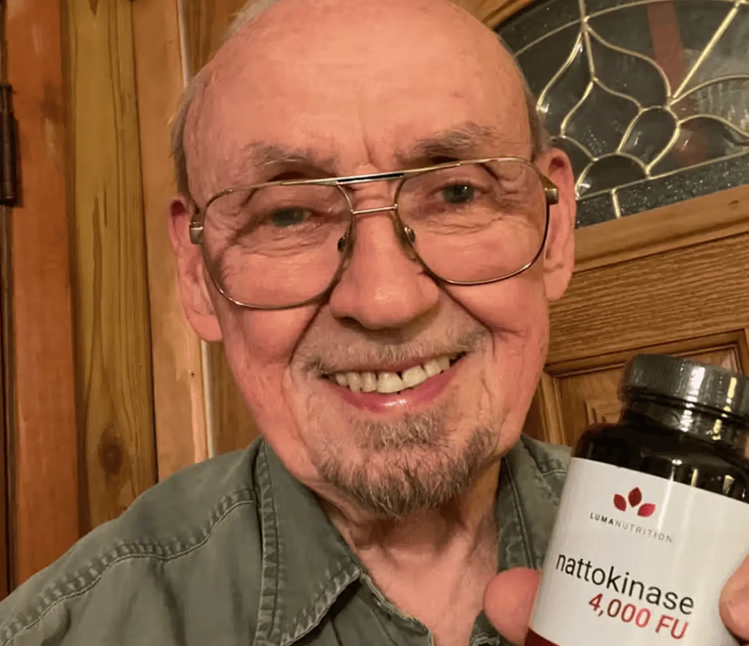 Elderly man smiling while holding a bottle of nattokinase supplement.